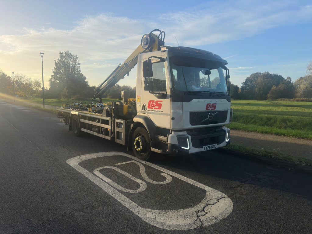 C&S Motor Group white Volvo flatbed recovery truck with crane parked on a road at sunrise, next to a 20 mph speed marking.
