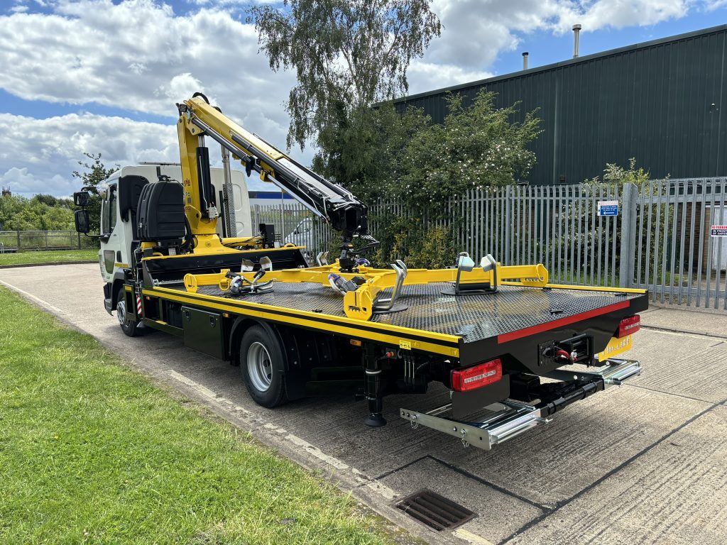 White flatbed lorry with yellow hydraulic crane and specialized lifting platform parked in an industrial yard.