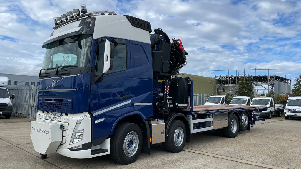 Blue crane-lorry loader truck parked in an industrial yard with hydraulic crane.